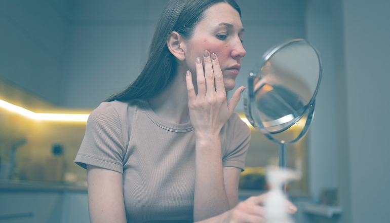 mujer mirandose al espejo con la mano tocandose una herida de la cara, un daño estetetico dertivado de un accidente de tráfico que merece indemnizacion por daños estetico tras accidente de tráfico